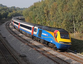 Engine with passenger carriages approacing on a left turn flanked by a stand of trees taken from an overbridge