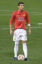 Cristiano Ronaldo – wearing a long-sleeved red jersey, white shorts with a number 7 on the left-leg side and a white armband on the left arm – prepares to take a free kick.