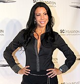 American television personality Danielle Staub posing for a camera in front a white step-and-repeat.