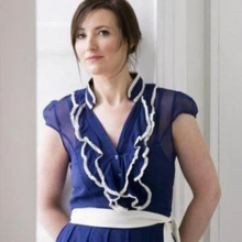 A photograph of Irish singer Margaret Healy wearing a blue dress and white belt. It is set against a white background.