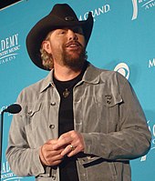 A bearded man wearing a grey shirt and a black cowboy hat