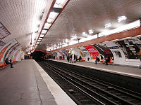 Photographie d'un quai souterrain, avec murs et plafond faïencés en forme d'arche