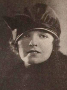 A young white woman wearing a dark fabric cap with brim low over her brows, and a dark coat or wrap