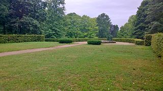 Fläche des ehemaligen Palais mit Hecke, die Lage und Umriss kennzeichnet. Mittig hinter dem Brunnen stand der ausgesetzte halbrunde Erker