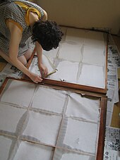 Person soaking water into the glue lines of a paper-covered shoji, from the paper side (frame hidden below)