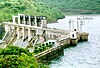 a large concrete dam holds back a lake, with green hills in the background