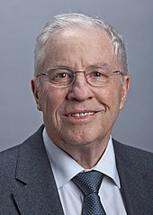 Portrait photographique d'un homme aux cheveux gris portant des lunettes.