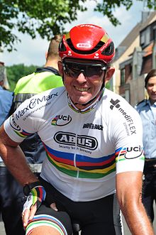 Man in white jersey with rainbow bands and a red helmet.