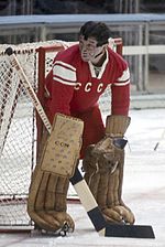 An ice hockey goaltender wears a facemask and covers the right side of the goal, looking to his right