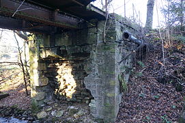 Une ancienne passerelle en métal portée par un mur de pierres disloquées.