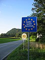 Two road-signs on the side of an open stretch of a two-lane highway. A Schengen internal border crossing marked only by a blue sign indicating the country being entered. The smaller white sign announces entry into the state of Bavaria.