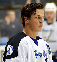 Head and shoulders of a hockey player in white and blue uniform, without his helmet on