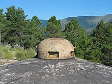 Photo d'un cuirassement bombé dépassant du béton, percé de plusieurs créneaux.