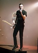 The Killers frontman Brandon Flowers sings onstage dressed in black.