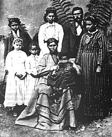 Portrait of six people standing around a seated woman holding a baby