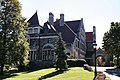 Side view of a stone mansion with a dark roof, four visible chimneys, and a drive-though arch