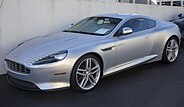 A front three-quarters view of a silver 2013 facelift DB9 in a dark environment.