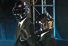Daft Punk wearing black suits on a red carpet.