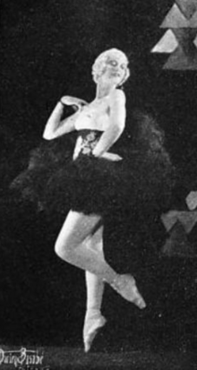 Harriet Lundgren, a white woman with light skin and hair, wearing a black Ballet costume and posing en pointe