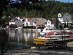 Foto von mehreren weißen Holzwohnhäusern, die an einem Gewässer liegen. Im Vordergrund befinden sich Boote.