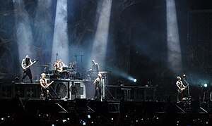 Rammstein performing in August 2013; upper level (left to right): Oliver Riedel, Christoph Schneider, and Christian Lorenz; lower level (left to right): Paul Landers, Till Lindemann, and Richard Kruspe