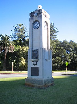Grey obelisk with a clock on each face, surrounded by roads and then trees
