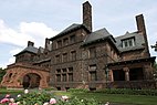 A reddish-brown three-story stone mansion with several high chimneys, photographed from a low angle.