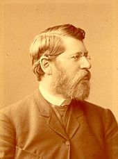 A sepia-tinted black and white portrait of a bearded man with glasses looking right