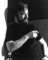 Greyscale image of Stephen Sondheim in a black t-shirt, looking to his left and holding a cigarette in his right hand.