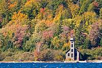 Small lighthouse standing on the lakeshore in front of trees in fall colors