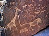 A dark brown limestone slab littered with rock engravings in light brown. The engravings all show African animals, with a large giraffe on the left. At the centre is a fantasy creature of a lion with human toes and an impossibly long tail. At the tip of the tail there is a pug mark with six toes.