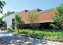 Northeast, a brick and glass building with metal siding on its far end and a stepped roof, on a sunny summer day