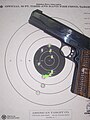 Handgun and paper target showing grouping of ten shots