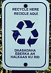 A rectangular sign with rounded corners, text about recycling, and the recycling symbol