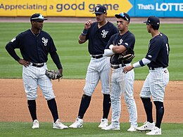 Four baseball players wearing navy blue jerseys with white pinstriped pants standing on a baseball field