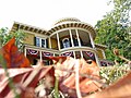 House with a round protruding porch with white columns and red-white-blue banners; red leaves in foreground