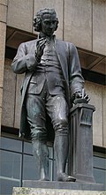 Statue of a man with a mortar and pestle in his left hand and his right-hand upraised.