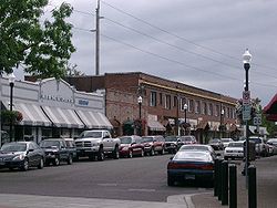 Photograph of a commercial street with four buildings along the far side, three 1-story and 1 2-story.