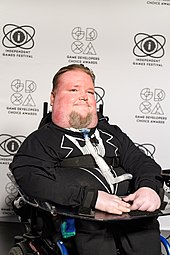 A man seated in a wheelchair, facing to the right of the camera.