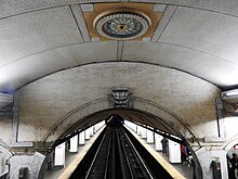 Detail of the station's ceiling with a circular light on the ceiling. The platform extension and its low ceiling are in the distance,