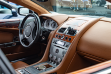 Cockpit of the left-hand drive Aston Martin DB9, featuring a black steering wheel and centre console, while the rest of the interior is a cocoa brown.