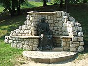 Gray outdoor statue of seated man, surrounded by white stone alcove