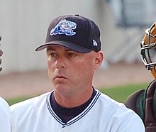 A man wearing a white baseball jersey and navy-blue baseball cap pictured from the shoulders up