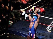Color photo of a masked wrestler lifting a smaller masked wrestler over his head.