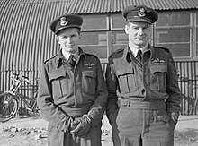 Deux officiers, en uniforme d'aviateur, debout, l'un croisant les mains et l'autre les ayant en poche.