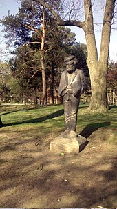 grey stone statue of man in front of grassy area and trees
