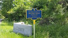 a picture of the marker with the gray, triangular, cement trough, the date 1917 in it side, behind