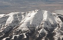 A snowcapped mountain with two clusters of communications towers at its peak