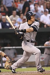 A baseball player following through on a swing. The player is wearing a gray uniform and navy baseball helmet; the uniform has a navy blue "NEW YORK" on the front, and the helmet has a white interlocking "N" and "Y" logo.