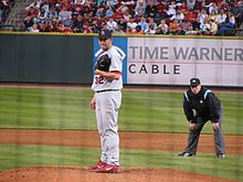 A man in a white baseball uniform and red baseball cap wearing a black baseball glove on his left hand